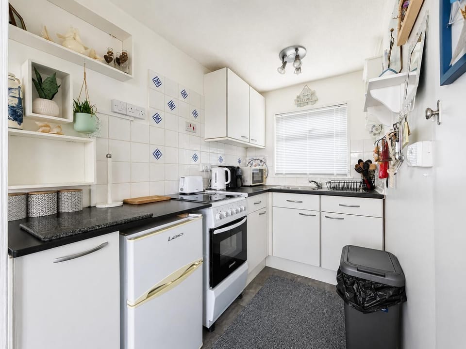 Practical kitchen featuring an electric oven, hob, microwave and fridge with freezer compartment.