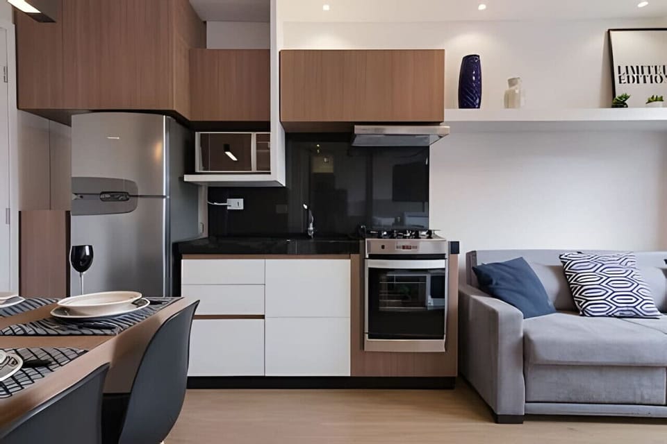 Sala/Cozinha - Sofá 2 lugares, fogão, micro-ondas, forno, exaustor, pia, armários, geladeira e mesa 4 lugares.