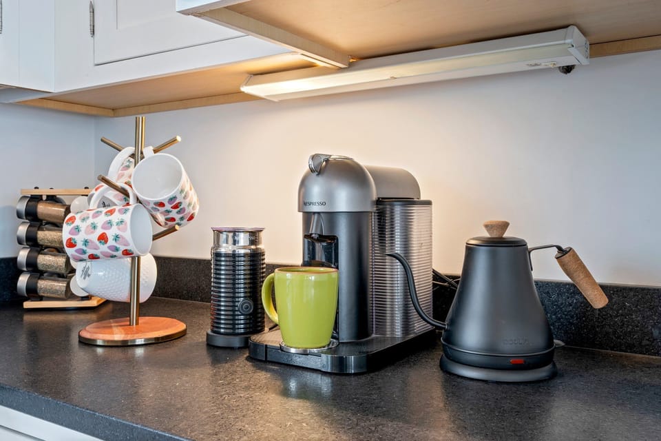 Kitchen with coffee maker, kettle, and colorful mugs, on black counter.