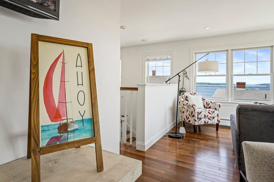 Water-view room with sailboat art, patterned armchair.