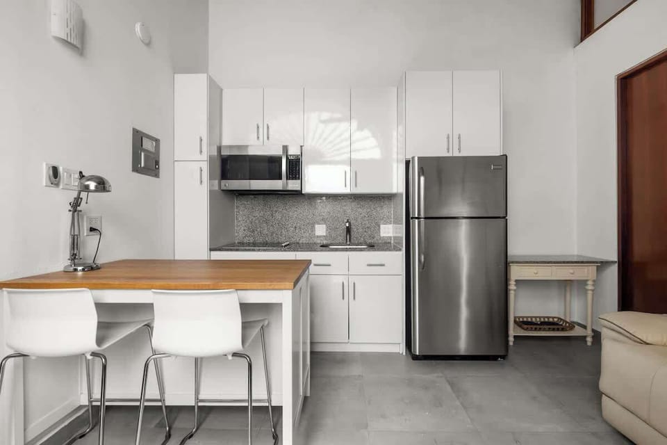 open kitchen with stainless steel fridge, air conditioner, livingroom with sofabed, seats, ceiling fan, microwave,  reading lamps, cabinets