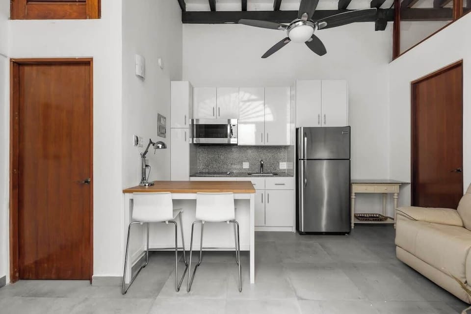 open kitchen with stainless steel fridge, air conditioner, livingroom with sofabed, seats, ceiling fan, microwave,  reading lamps, cabinets