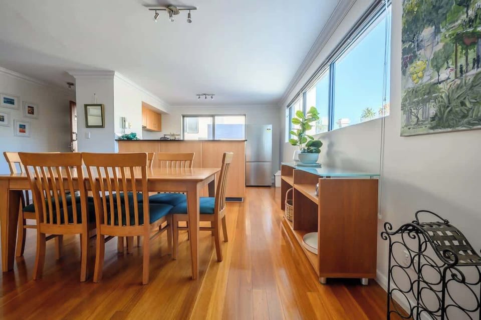 Settle into our cozy living space, where warm wooden floors beautifully complement the dining area. Large windows invite natural light, creating a bright and welcoming atmosphere, and the nearby kitchen with a refrigerator ensures convenience for you