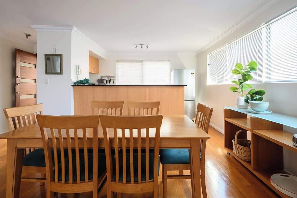 Gather around our inviting dining table, comfortably seating six, set on a warm wooden floor that perfectly complements the rich timber. Enjoy meals in this bright space, featuring large windows and a convenient refrigerator nearby.