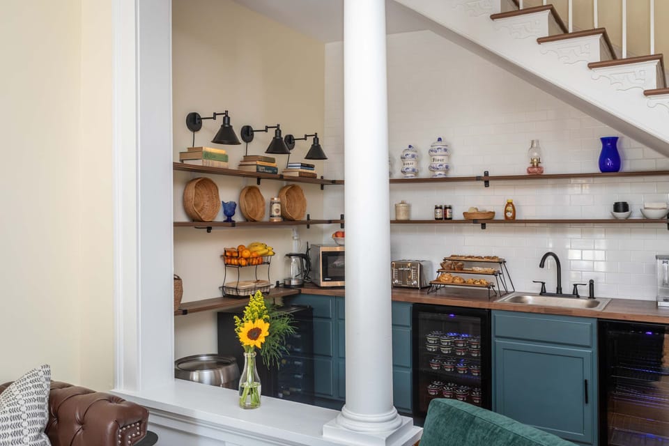 Cozy kitchen with open shelving and modern appliances under a decorative staircase.