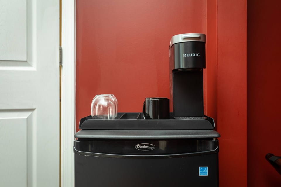 Compact coffee station with a Keurig machine and glassware against a red wall
