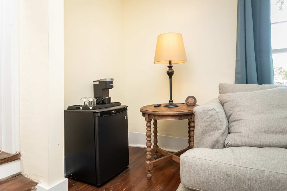 Cozy corner with a wooden side table, lamp, and coffee station next to a comfortable sofa.