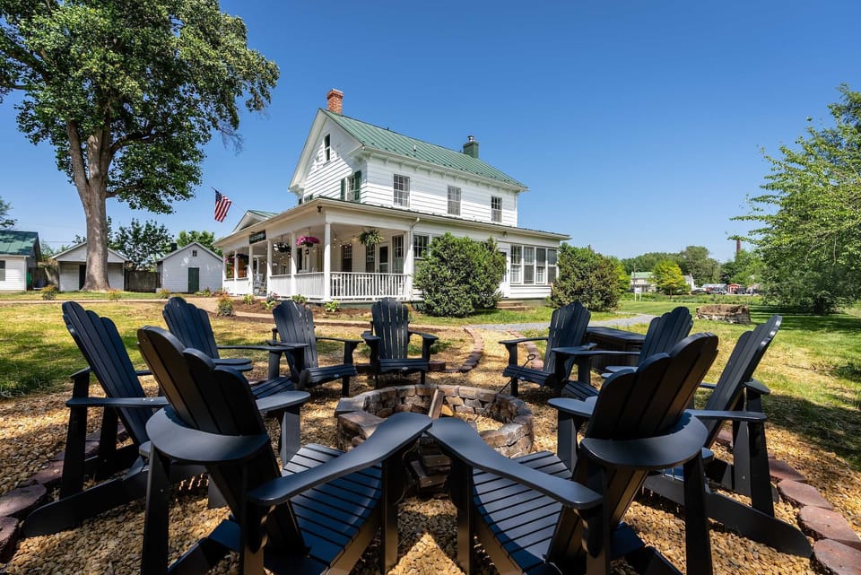 Outdoor fire pit area with seating in front of a classic white farmhouse.