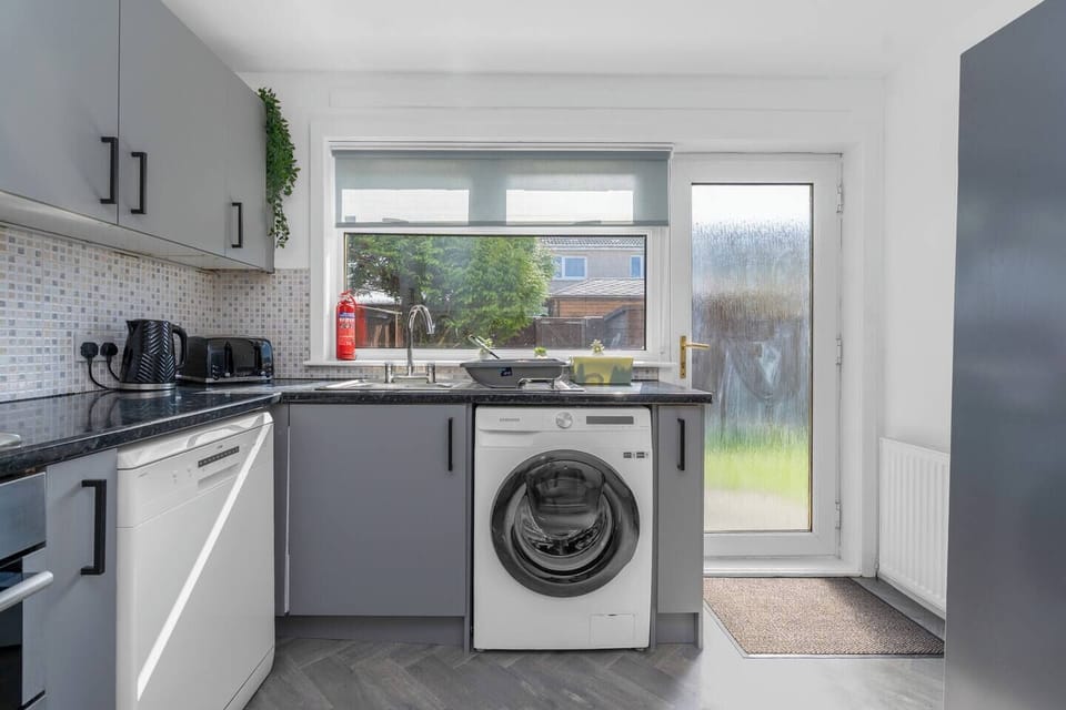 Bright and functional kitchen with modern appliances, including a washer, dishwasher, and direct access to the garden—perfect for easy living.