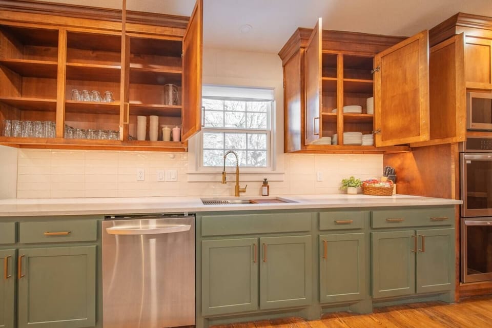 This fully stocked kitchen features open cabinets with neatly organized dishes and glassware, a sleek dishwasher, and a large window for natural light—perfect for home-cooked meals or extended stays.