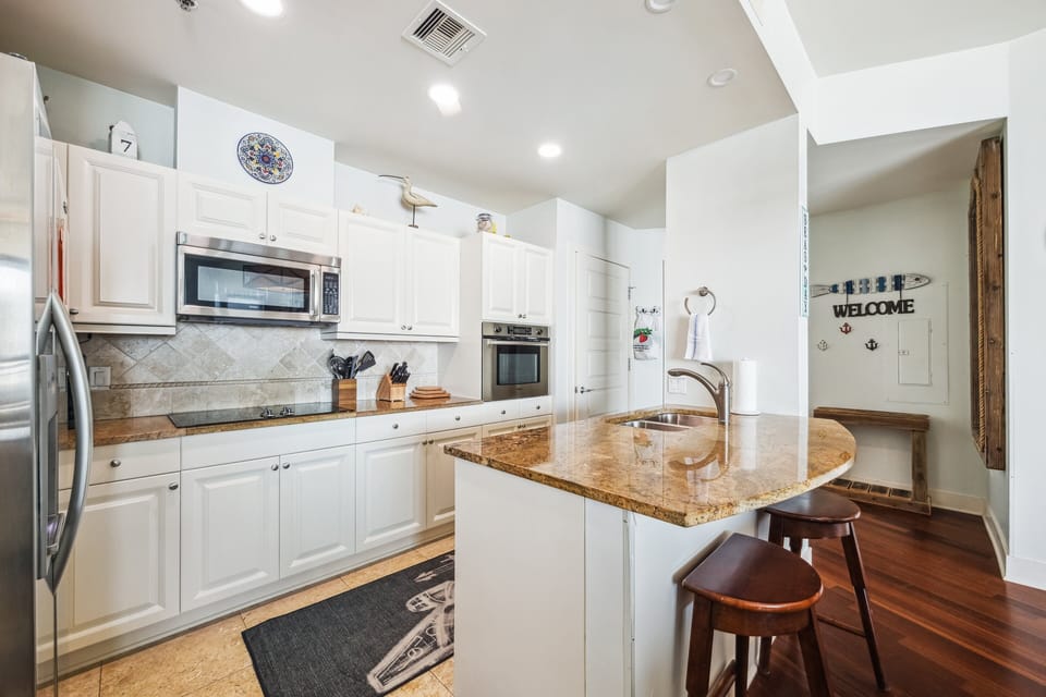 Bright coastal kitchen with granite counters, breakfast bar seating, and white cabinetry—perfect for relaxed dining at Palisade Palms.