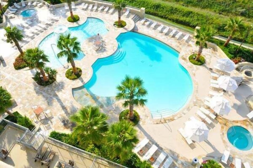 Resort-style pool deck with sparkling pools, hot tub, loungers, and tropical landscaping. Enjoy sun-soaked relaxation, shaded umbrellas, and family-friendly amenities just steps from the beach.