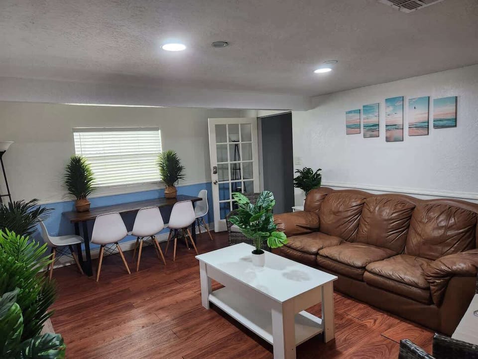 Bright and inviting living space with a cozy leather sofa, modern dining table, and tropical plants. Ideal for relaxation and productivity.