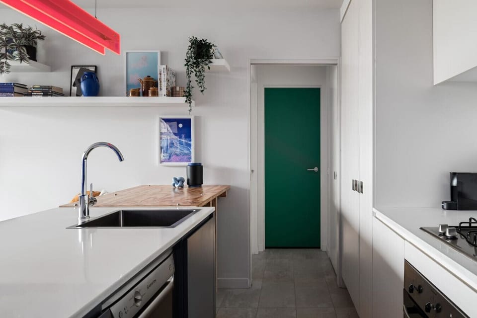 This bright and modern kitchen features sleek appliances, bold pops of color, and open shelving with curated decor—perfect for cooking and entertaining in style