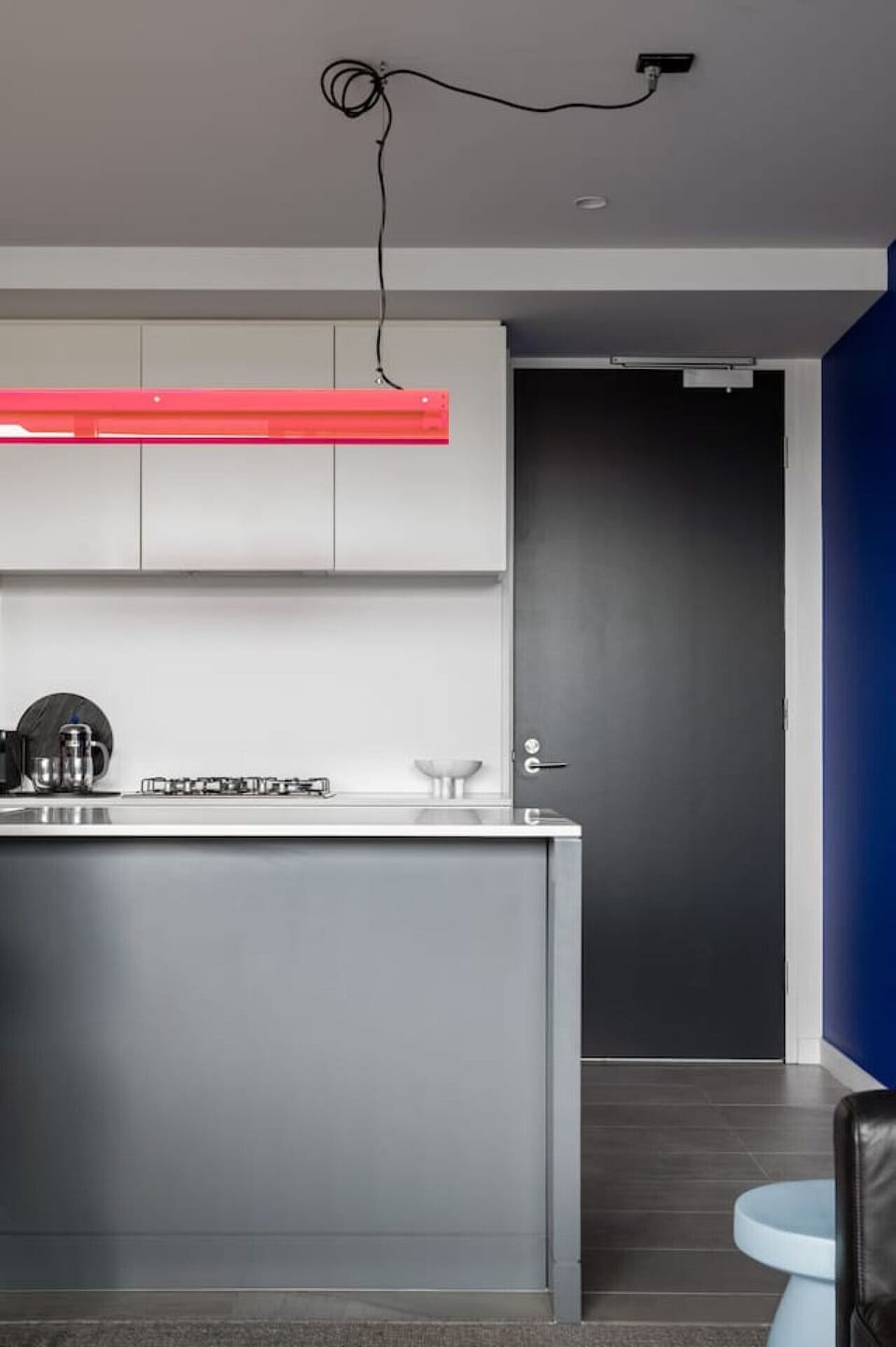 This modern kitchen features sleek finishes, a gas cooktop, and a bold designer light fixture, all set against a vibrant and stylish color palette