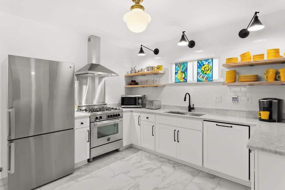 Bright, fully equipped kitchen with stainless appliances, open shelving, and playful stained glass. Cook on a premium gas range and enjoy a modern coffee setup.