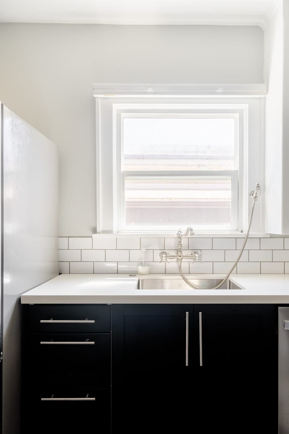 Kitchen sink beneath a window beside a refrigerator.