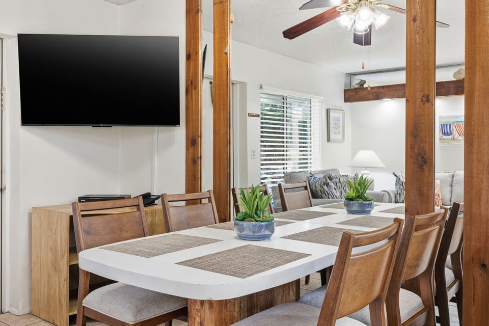 A bright dining space features a large table with seating, positioned beside the living area for easy meals and gatherings.
