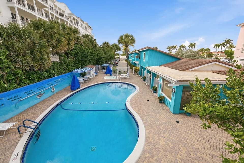 An aerial view shows a winding pool bordered by tropical foliage, lounge chairs, and striped umbrellas at Sand Dune Shores.