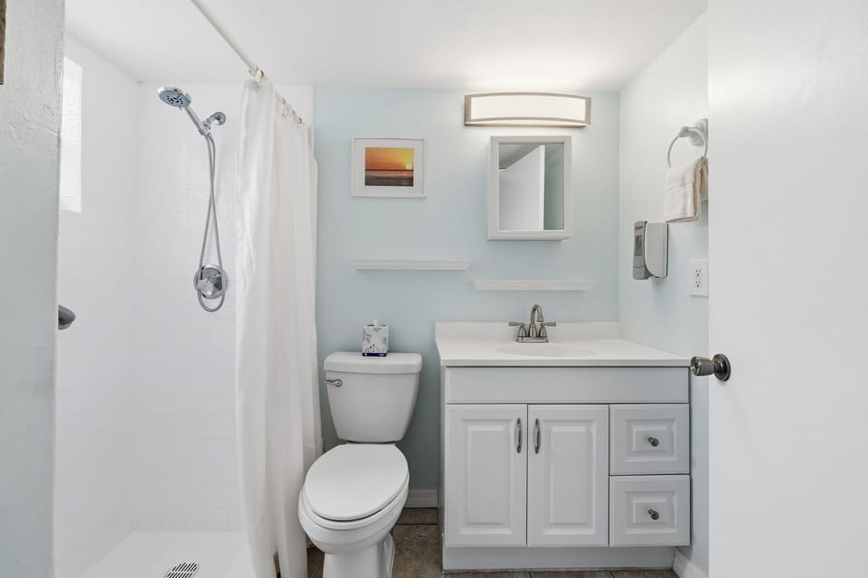 The bathroom features a vanity with storage, a shower, and soft blue walls for a clean and refreshing feel.