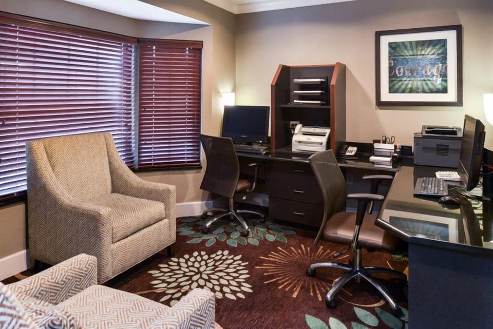 Lounge seating area with plush chairs, vibrant carpet, and natural light filtering through the blinds