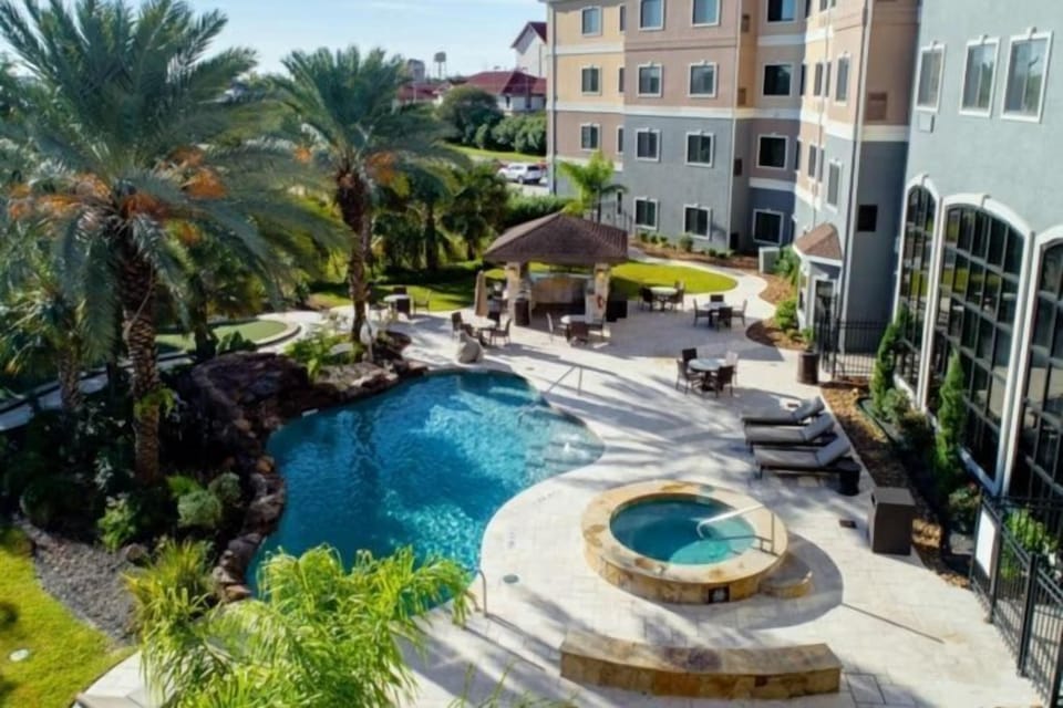 Outdoor pool and hot tub surrounded by palm trees and lounge seating