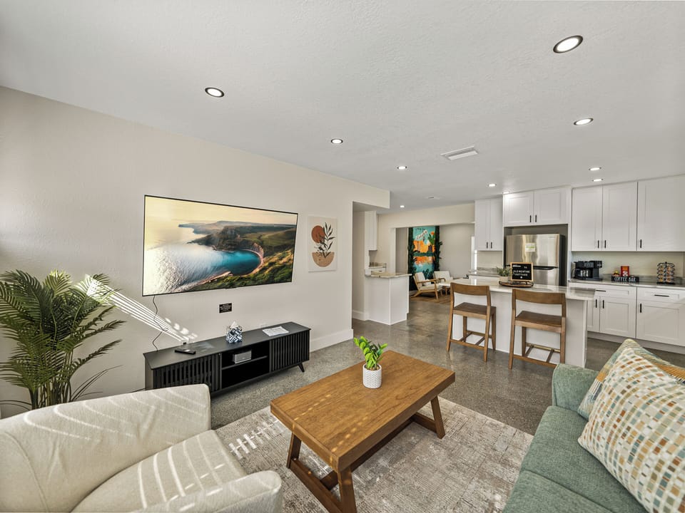 This modern living room features earth-toned decor, large windows for natural light, and cozy seating, including a swivel chair. A 65" TV is perfect for movie nights, while natural materials and soft lighting create a serene, inviting atmosphere. 