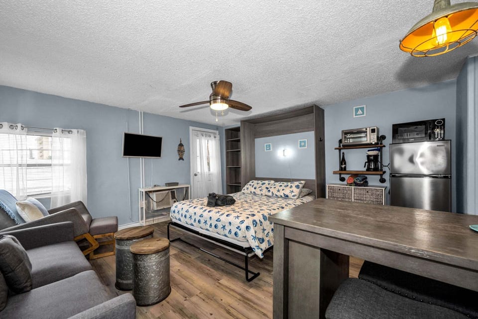 The full studio layout showcases smart space-saving design — Murphy bed, dining table, kitchenette, and lounge area all within easy reach, just steps from Clearwater Beach.
