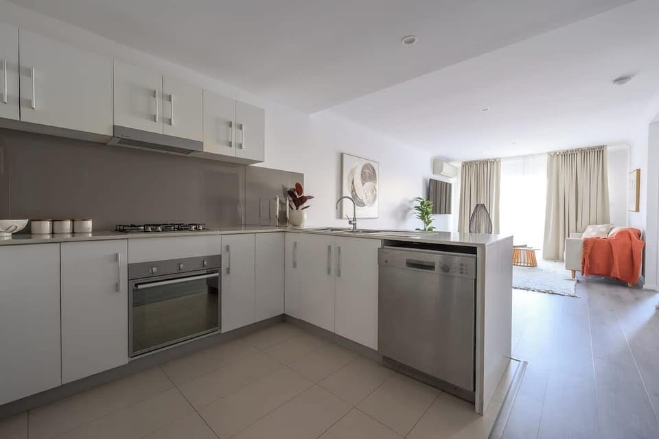 This sleek L-shaped kitchen features premium stainless steel appliances, including a dishwasher and gas cooktop. The open-plan design flows seamlessly into the light-filled living area, making it perfect for entertaining while you cook.