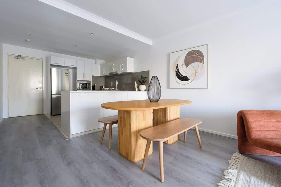 This open-plan space features a stunning wooden dining set with bench seating, flowing into a sleek white kitchen with stainless steel appliances. Perfect for enjoying home-cooked meals in a beautifully curated setting.