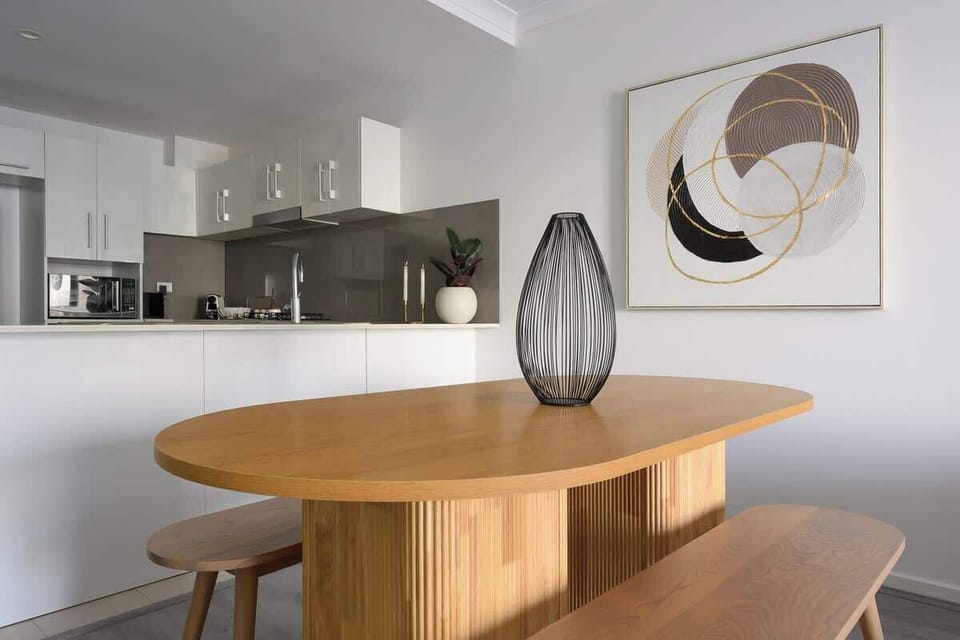 Elevate your stay in a space where organic textures meet modern art. Featuring a smooth wooden dining bench, clean white cabinetry, and sophisticated decor accents, this area is as functional as it is stylish.