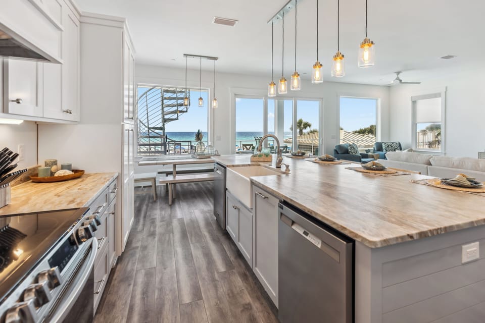 Cook with ocean views streaming through expansive windows in this bright, modern kitchen featuring warm wood counters and stylish pendant lighting.