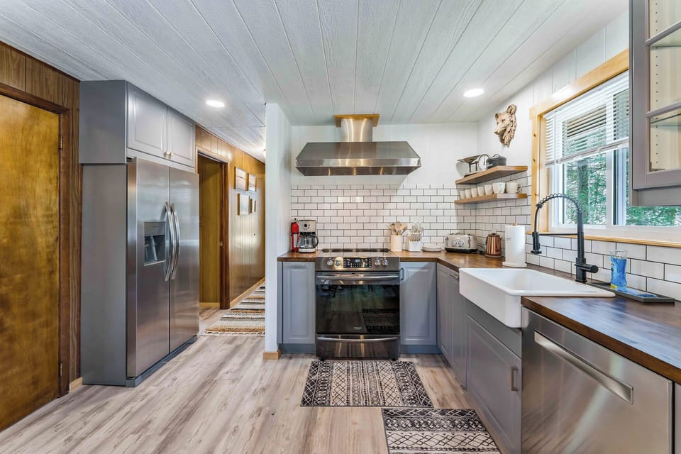 This kitchen seamlessly blends contemporary convenience with vintage flair. Sleek stainless steel appliances and a modern farmhouse sink are complemented by retro-inspired touches like the cream Haden toaster and copper kettle, creating a space that feels both fresh and timeless.