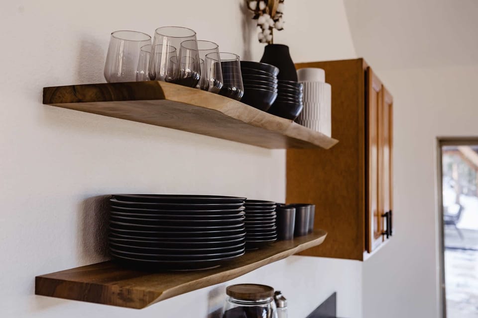 Open shelf for dishware with a variety of drinking glasses, more mugs, and wine glasses in the cabinet.