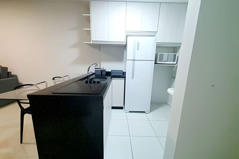 Cozinha - Mesa 2 cadeiras, fogão indução, pia, geladeira, micro-ondas e armários.
