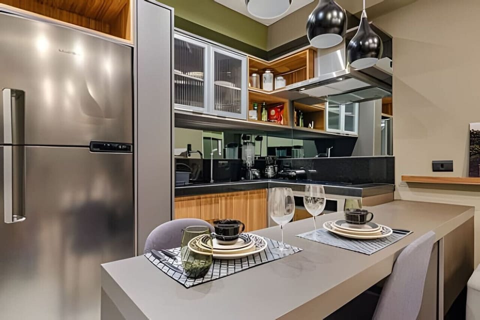 Cozinha moderna com geladeira, armários de vidro, bancadas pretas e um conjunto de café da manhã para dois com pratos, copos e utensílios de mesa.
