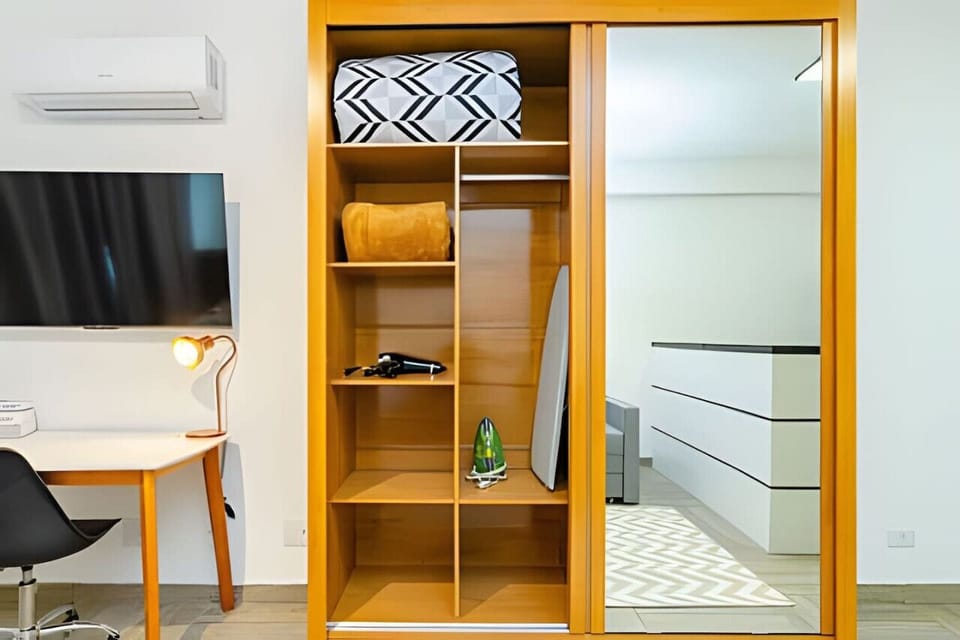 Armário com roupas de cama, secador de cabelo, tábua e ferro de passar.