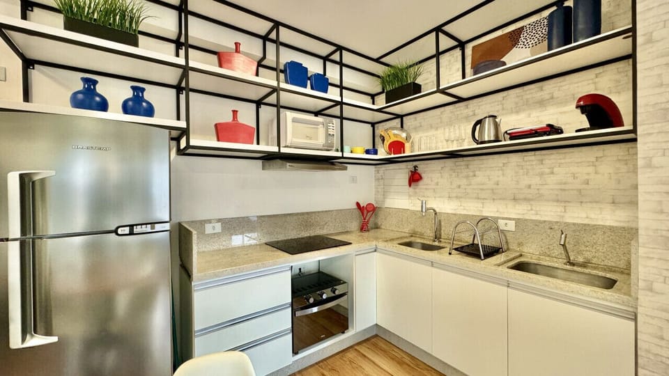 Cozinha com geladeira, cooktop 4 bocas, exaustor, micro-ondas, 2 pias, xícaras, grill, chaleira de inox e utensílios.