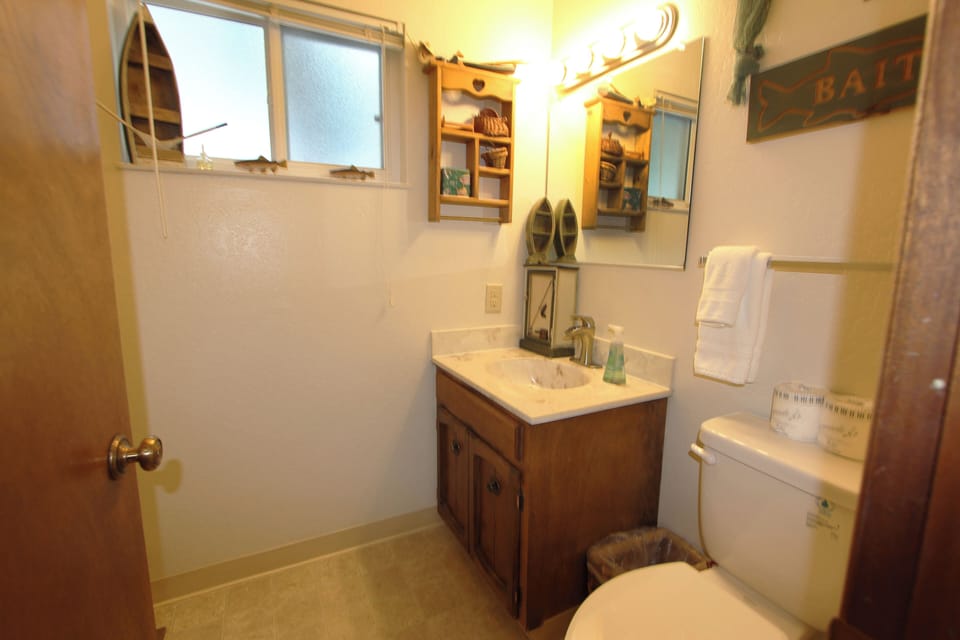 Bathroom with vanity, sink, mirror, toilet, towel rack, window, wall shelf, and vanity light.