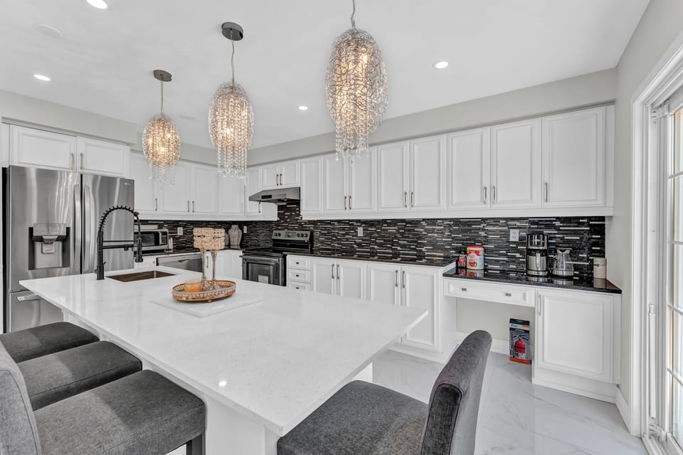 Bright kitchen with crystal lights, white cabinets, and sleek black backsplash.