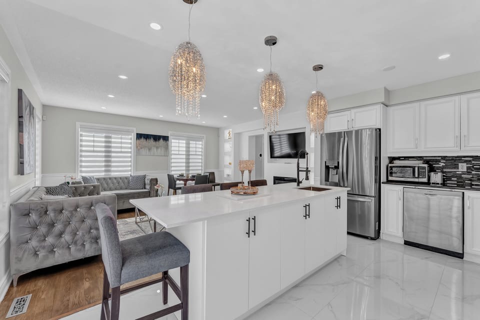 White kitchen island with crystal pendant lights and stainless steel appliances.