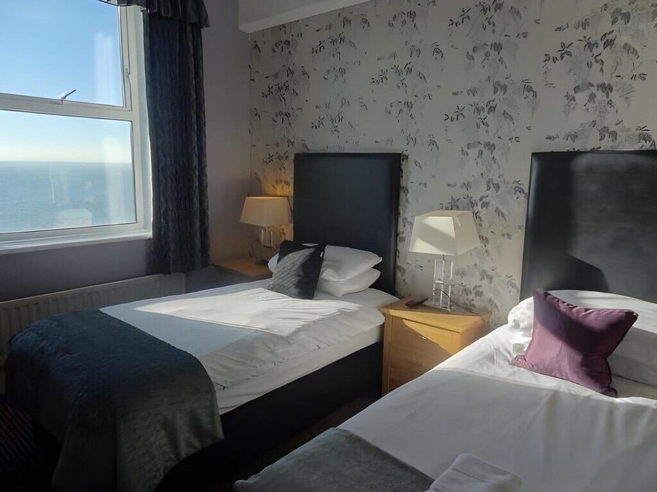 Wake to soft daylight and sea glimpses beside twin beds.