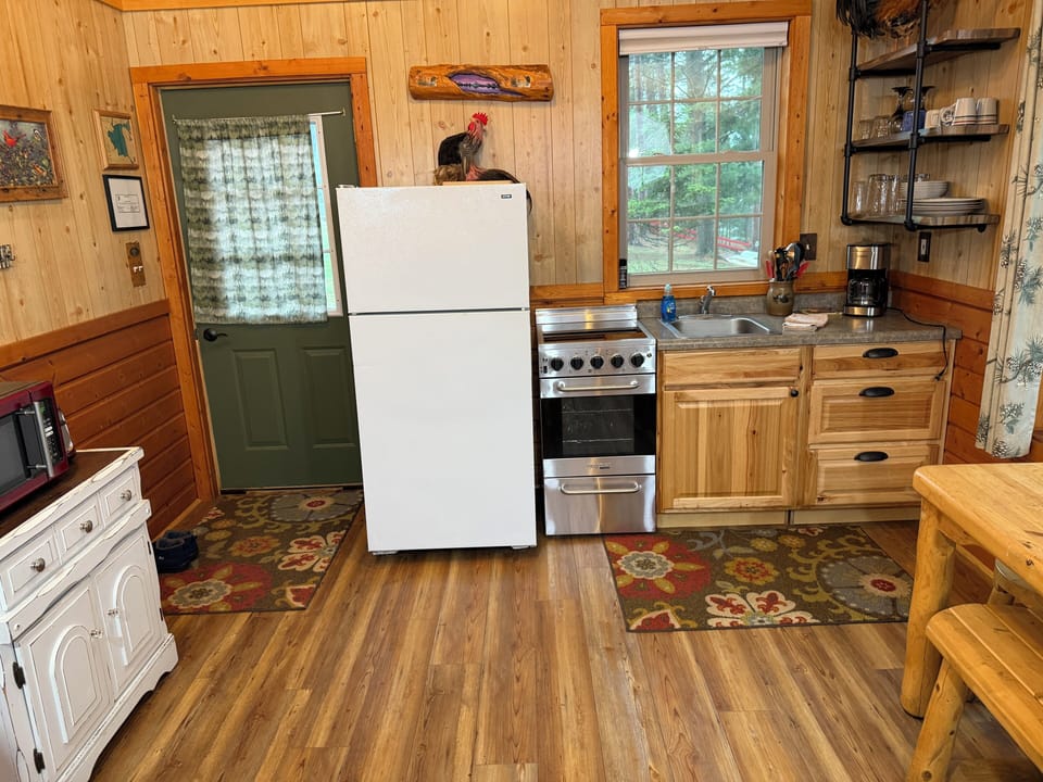 Your cozy cabin kitchen offers everything you need—a full-size fridge, stove with oven, sink, and ample counter space. Natural light pours in, and rustic wood details create a warm, homey feel perfect for preparing your favorite meals.