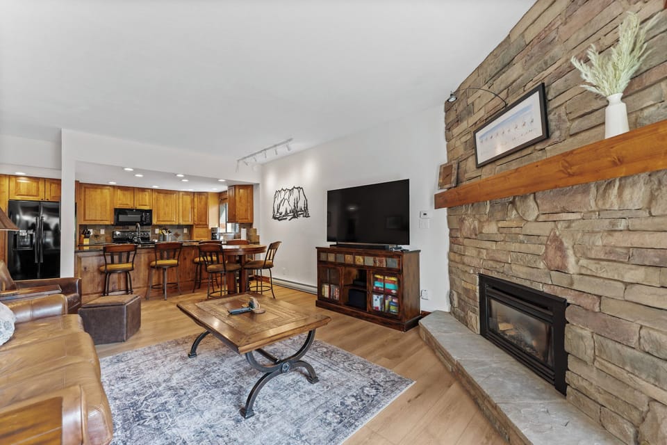 Living area with a large flat-screen TV, beautiful stone fireplace, queen sleeper sofa, and balcony access.