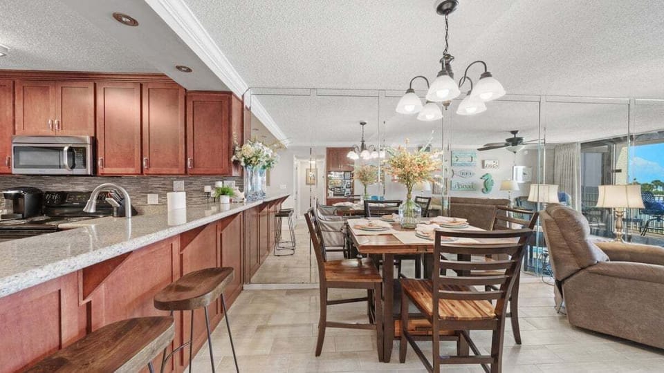 Open kitchen and dining area with wood cabinetry, coastal décor, spacious table, and granite breakfast bar with beach views.