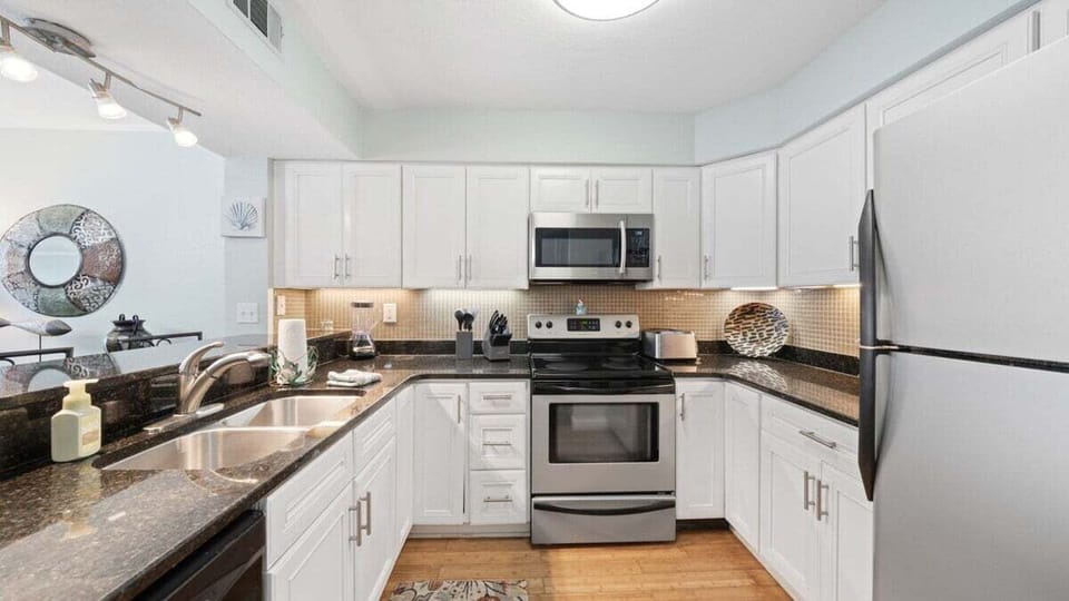 This fully equipped kitchen features sleek granite countertops, stainless steel appliances, and crisp white cabinetry.