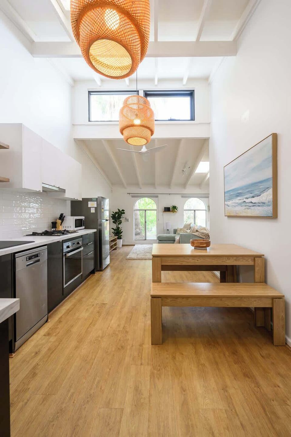 The modern kitchen offers a wooden table, oven, microwave, ample cabinets, stove, fridge, sink, and coffee maker. Flowing into the living space, you'll find a comfy sofa, plush rug, and bright windows—perfect for relaxation.