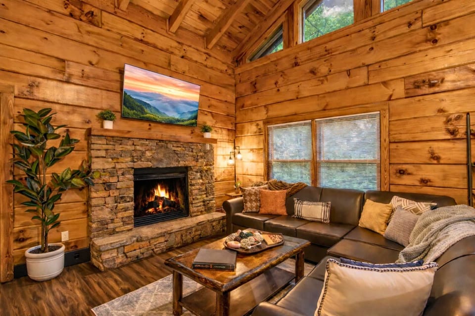 Unwind in rustic luxury – this warm and inviting living room features a stone fireplace, plush sectional seating, and soaring wood-paneled ceilings, perfect for relaxing after a day in the Smoky Mountains.
