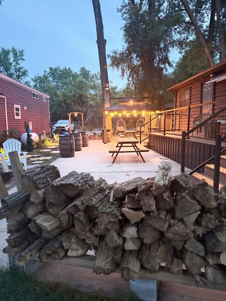 Outdoor deck with seating, two picnic tables, birdcage-style swings, and firewood for cozy evening fires.