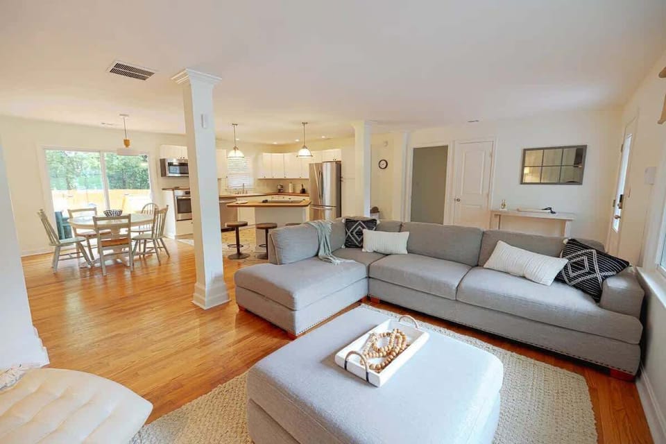 Relax in this spacious, sunlit living area with a cozy sectional and modern kitchen, perfect for family gatherings.